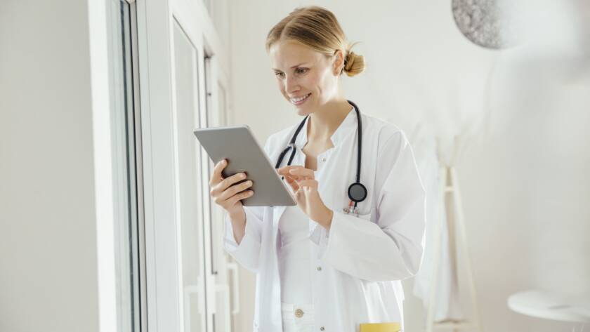 Ein Allgemeinmediziner in einem modernen Büro hält ein iPad mit einer professionellen Praxiswebseite, die Online-Terminvereinbarung, Patienteninformationen und Kontaktdaten anzeigt.