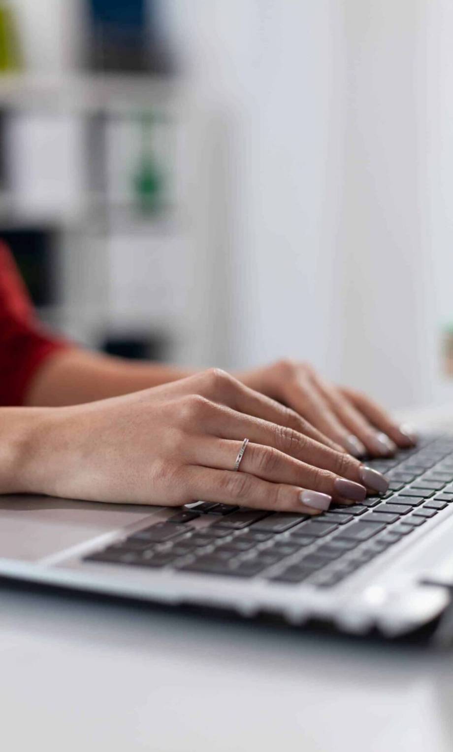 Hand einer Frau mit Ring tippt auf einem Laptop in einer Webdesign Agentur.